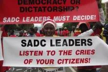 A protester holds up a poster that reads “SADC Leaders Listen to the cries of your citizens”. Above her, is a poster that reads “Democracy or Dictatorship? SADC leaders must decide!”