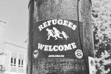 Black and white Refugees Welcome poster with a picture of a family running stuck to a pole.