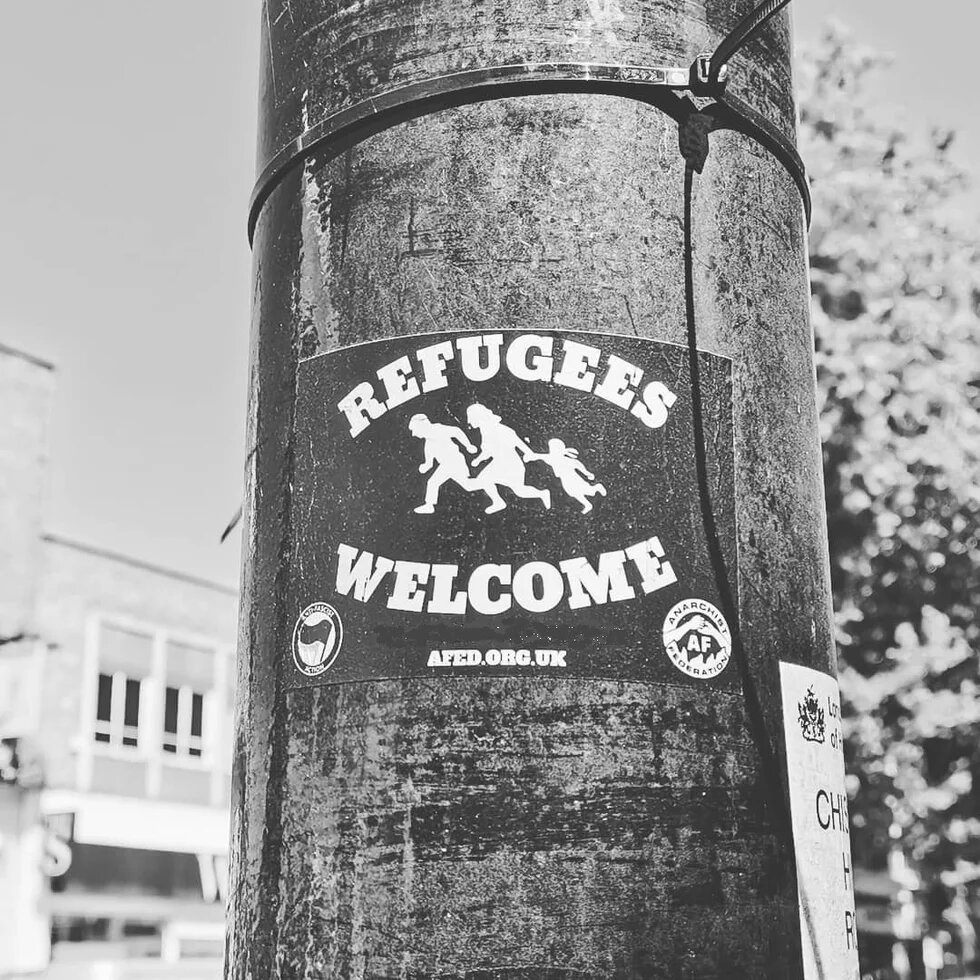 Black and white Refugees Welcome poster with a picture of a family running stuck to a pole.