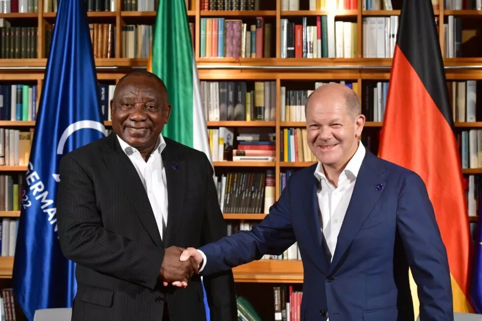 South African President Cyril Ramaphosa shaking hands with the German Chancellor Olaf Scholz with the Group of 7 Germany Presidency, South African and German flags behind them.